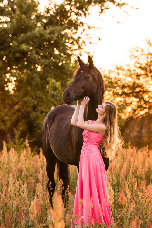 Mädchen im Kleid mit Pferd im Sonnenuntergang
